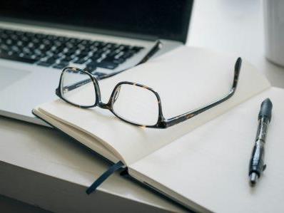 computer, quaderno appunti e occhiali su di un tavolo